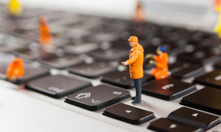 Conceptual image of miniature workmen repairing a laptop keyboard
